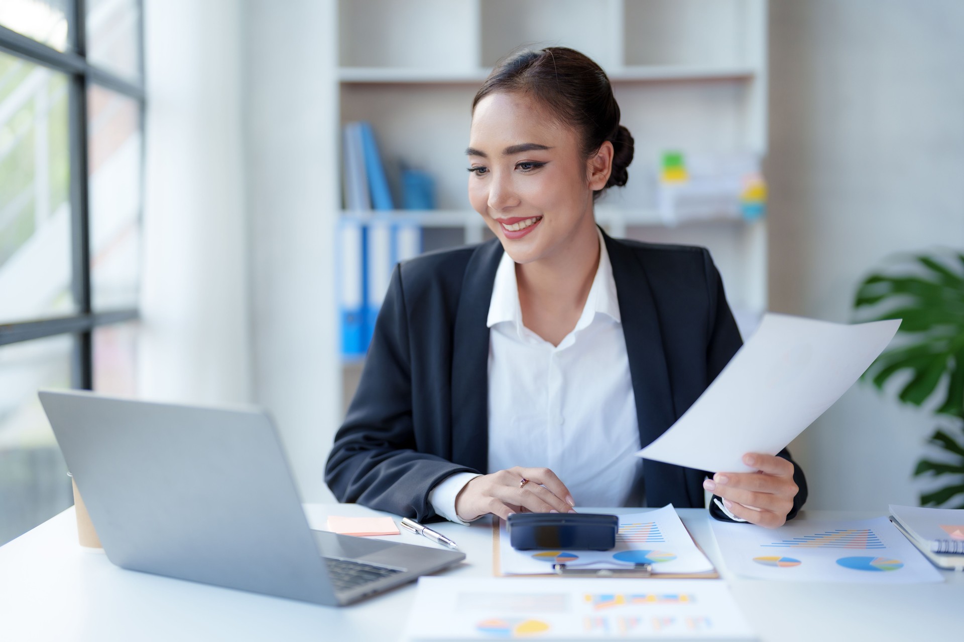 Beautiful Asian businesswoman working on paperwork at her desk in the office review work from different department, take minute of meetings report other document.